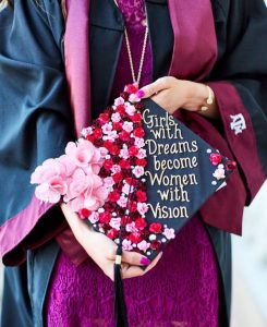 Graduate holding a decorated cap with inspiring quote at college graduation.