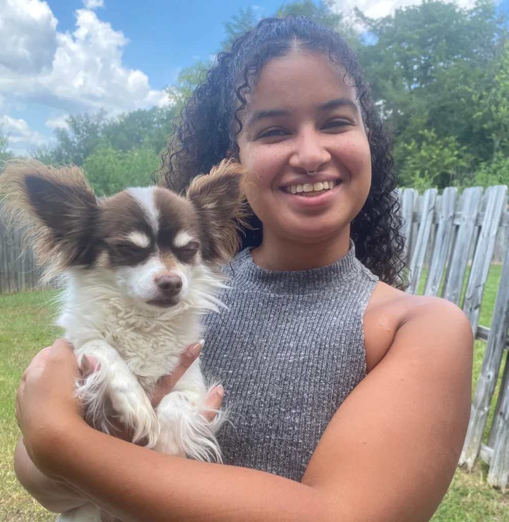Young woman holding a small Chihuahua dog outdoors on a sunny day.