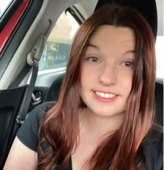 Young woman with long red hair smiling inside a car.