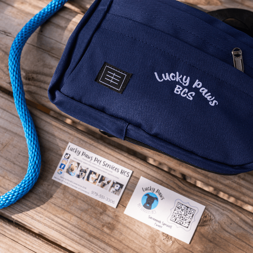 Lucky Paws BCS branded pet service bag and business cards on wooden surface.