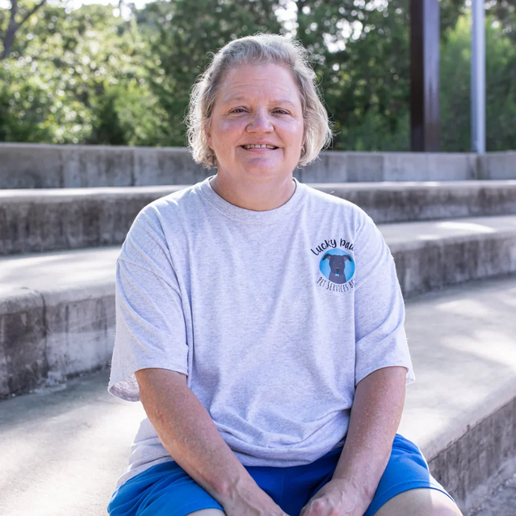 Happy team member at Lucky Paws BCS wearing company T-shirt outdoors.